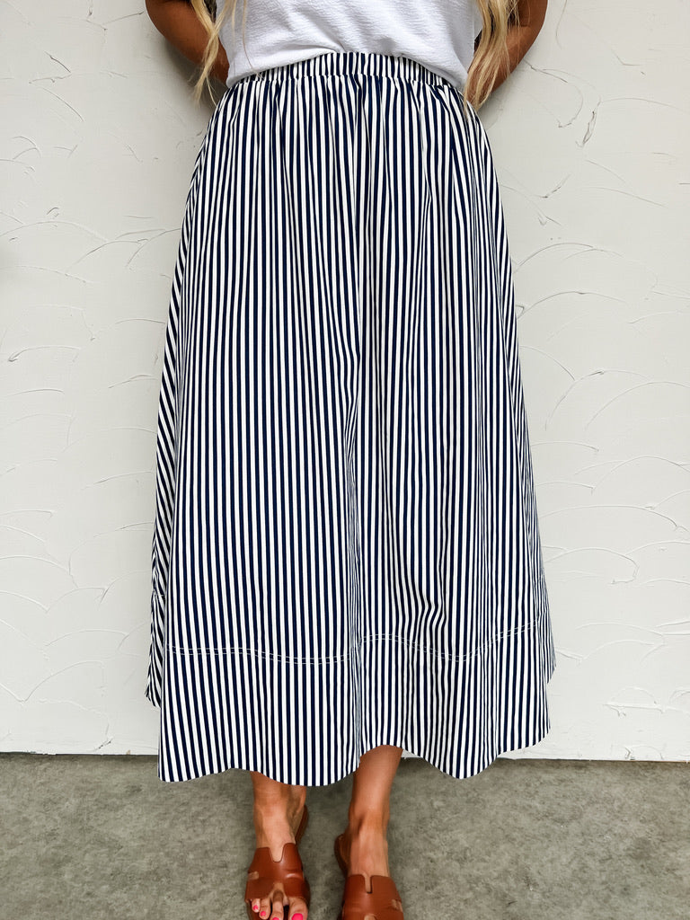 Person wearing a black and white striped skirt against a white wall.
