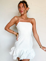 Woman wearing a white dress with a ruffle hem against a plain background