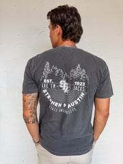 Man wearing a gray t-shirt with a graphic design on the back against a white wall.