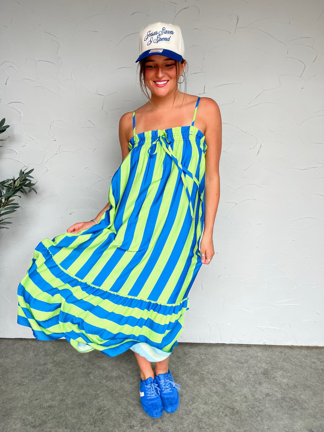 Person wearing a blue and green striped dress with a white cap against a plain background