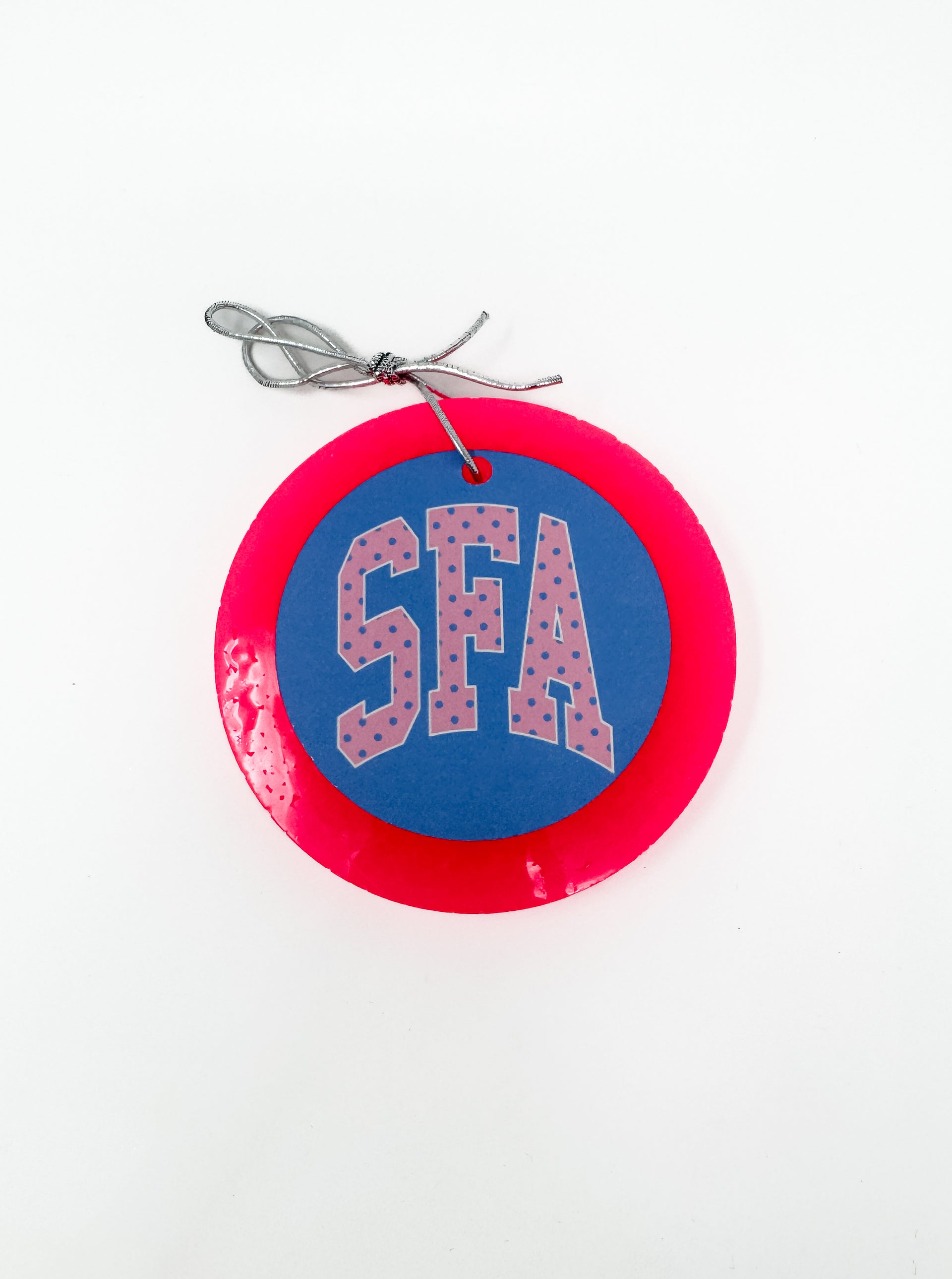 This "SFA" car freshie features a spirit-filled, round design with collegiate-style lettering in a polka dot pattern, all framed by a smooth, circular outer border. It comes ready to hang from your rearview mirror with an attached silver string. Scents vary.