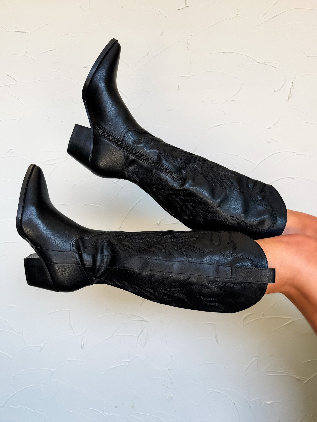 Black knee-high boots worn by a person on a light gray background