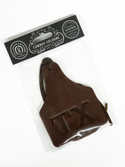 Brown leather air freshener cow tag with 'TEX' branding in clear packaging, featuring a 'Cowboy Cologne' label.