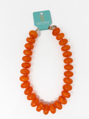 An orange beaded necklace with chunky, rounded disc-like beads, attached to a teal Taylor Shaye Designs brand tag, shown on a plain white background.