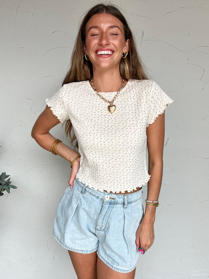 Woman wearing a white blouse with ruffled sleeves and denim shorts against a plain background