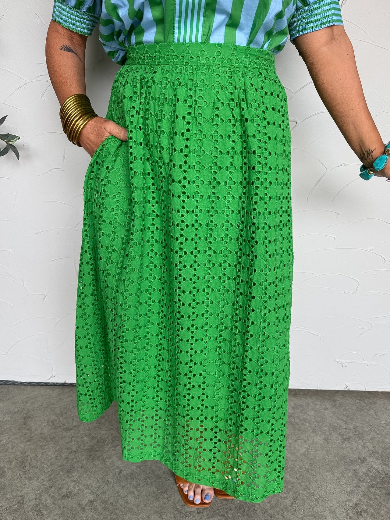 Person wearing a green eyelet skirt and striped shirt against a white wall.