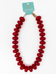 A red beaded statement necklace with large glossy oval beads, attached to a light blue Taylor Shave Designs card, shown on a white background.