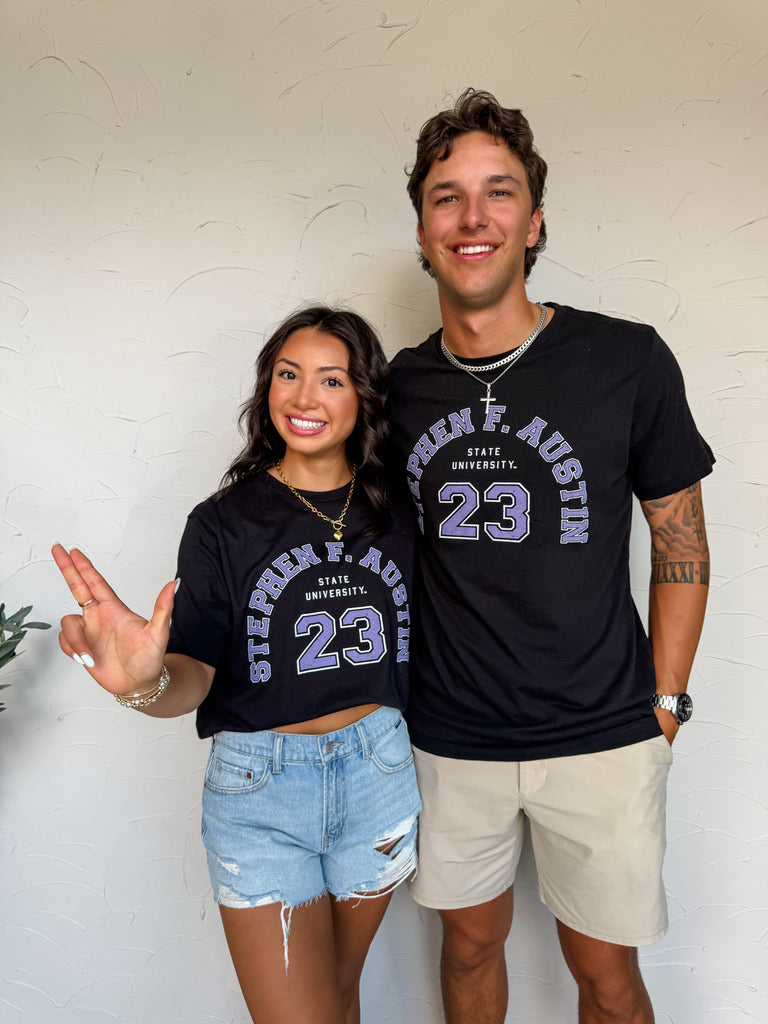 Two people wearing Stephen F. Austin State University t-shirts with the number 23 against a white brick wall.