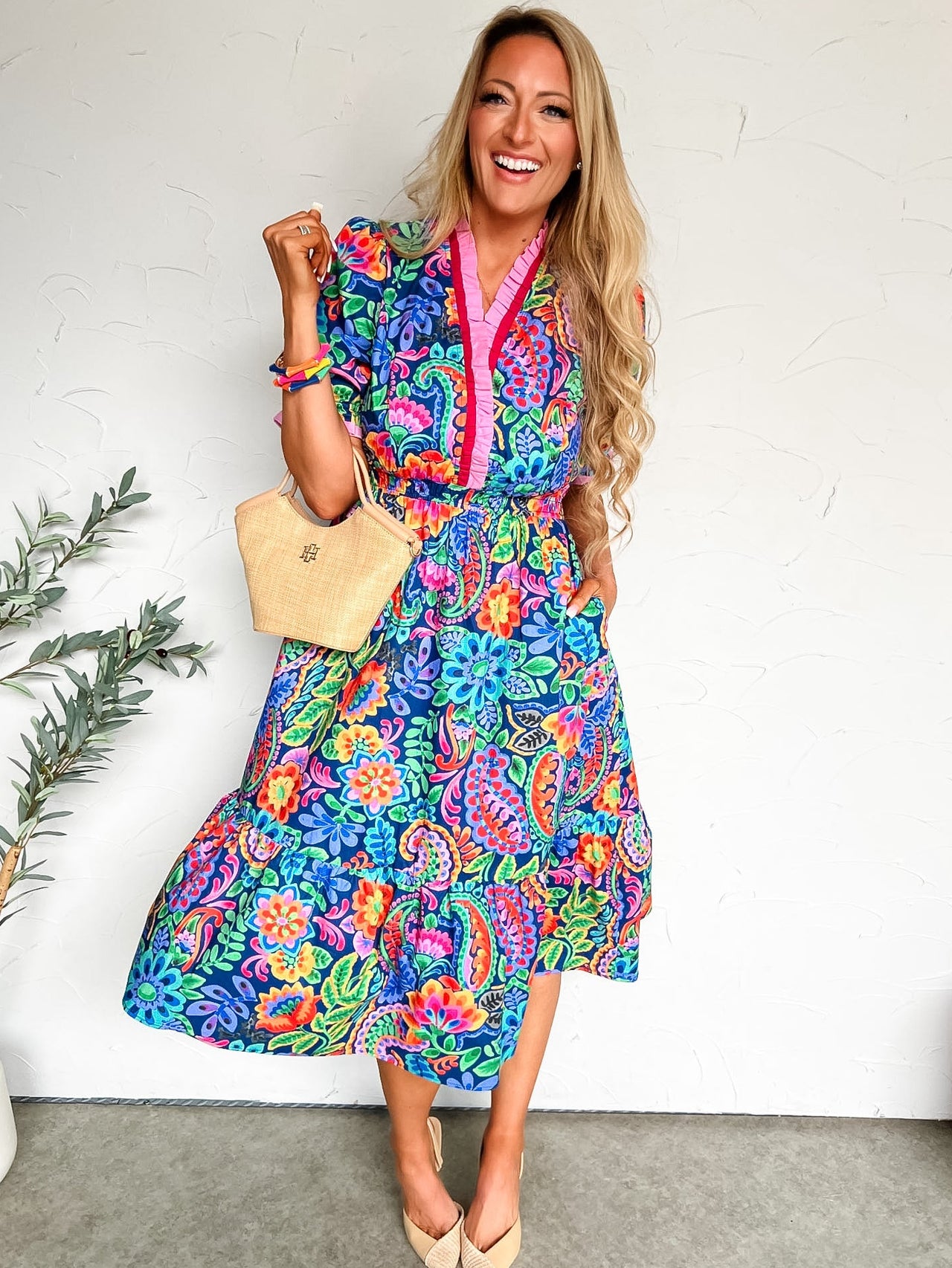 Woman wearing a colorful floral dress against a white wall.