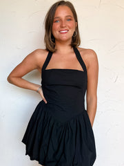 Woman wearing a black halter dress against a white wall
