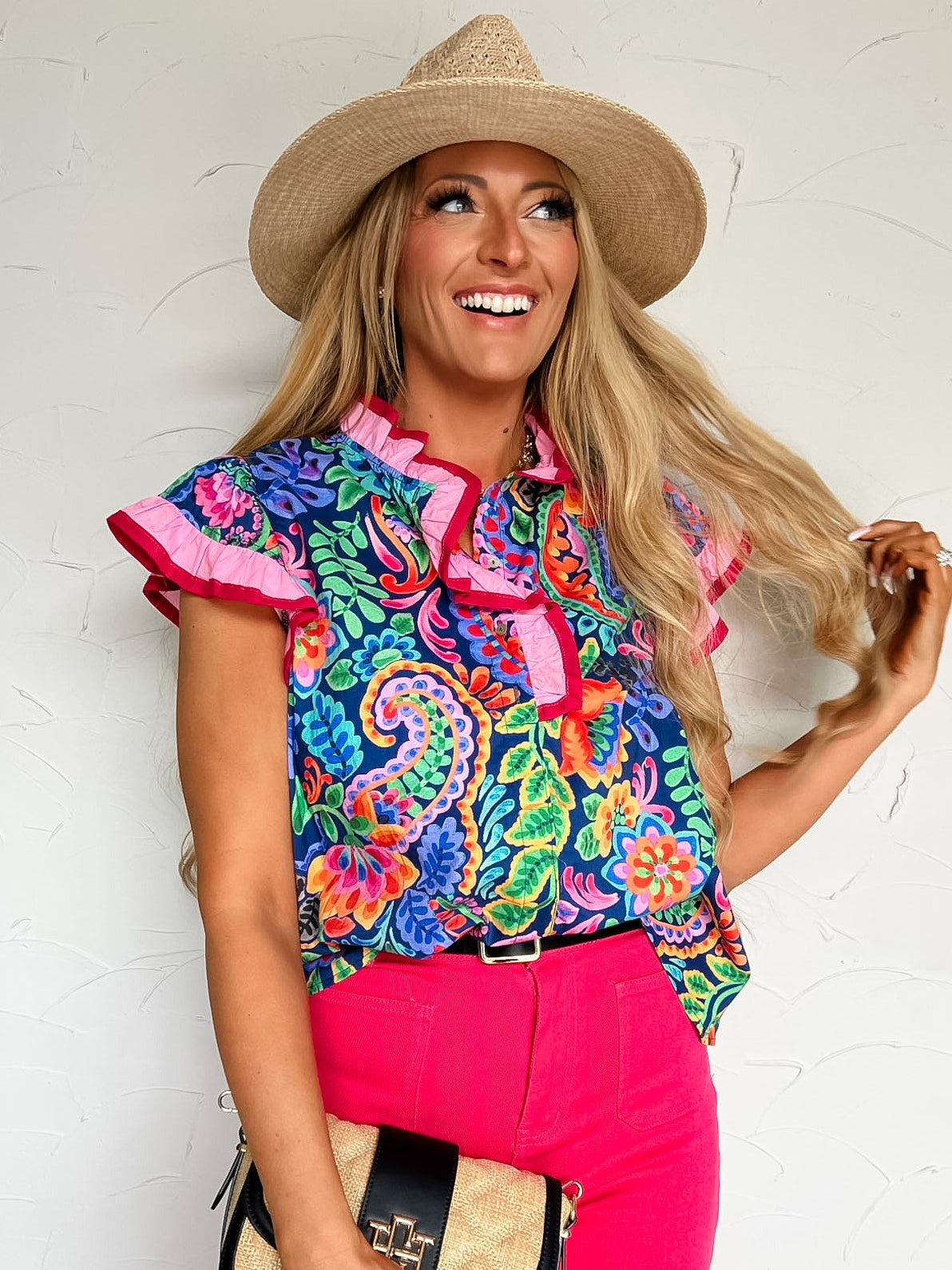 Woman wearing a colorful patterned shirt and pink pants with a straw hat against a white background