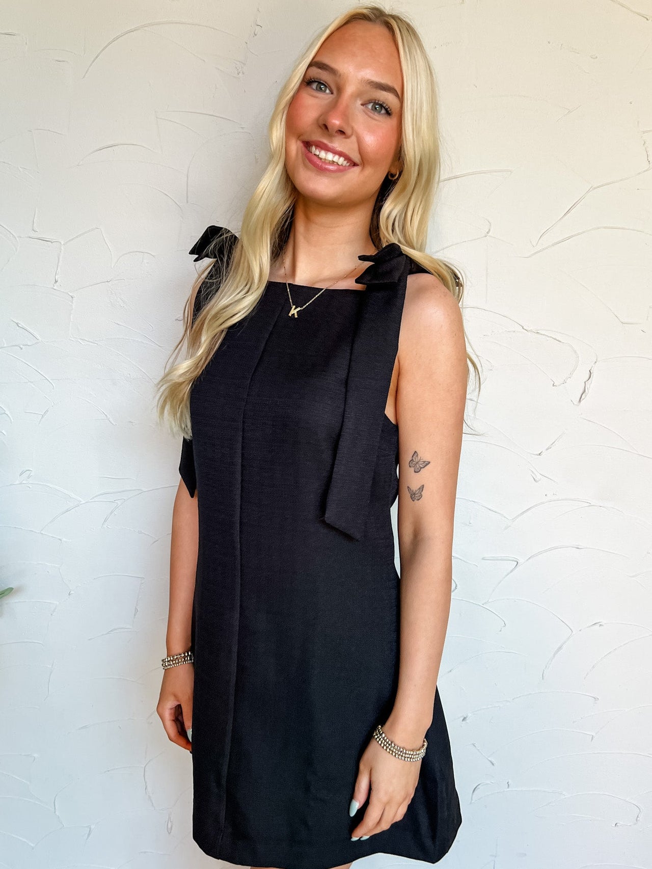 Woman wearing a black dress with bow details against a white wall