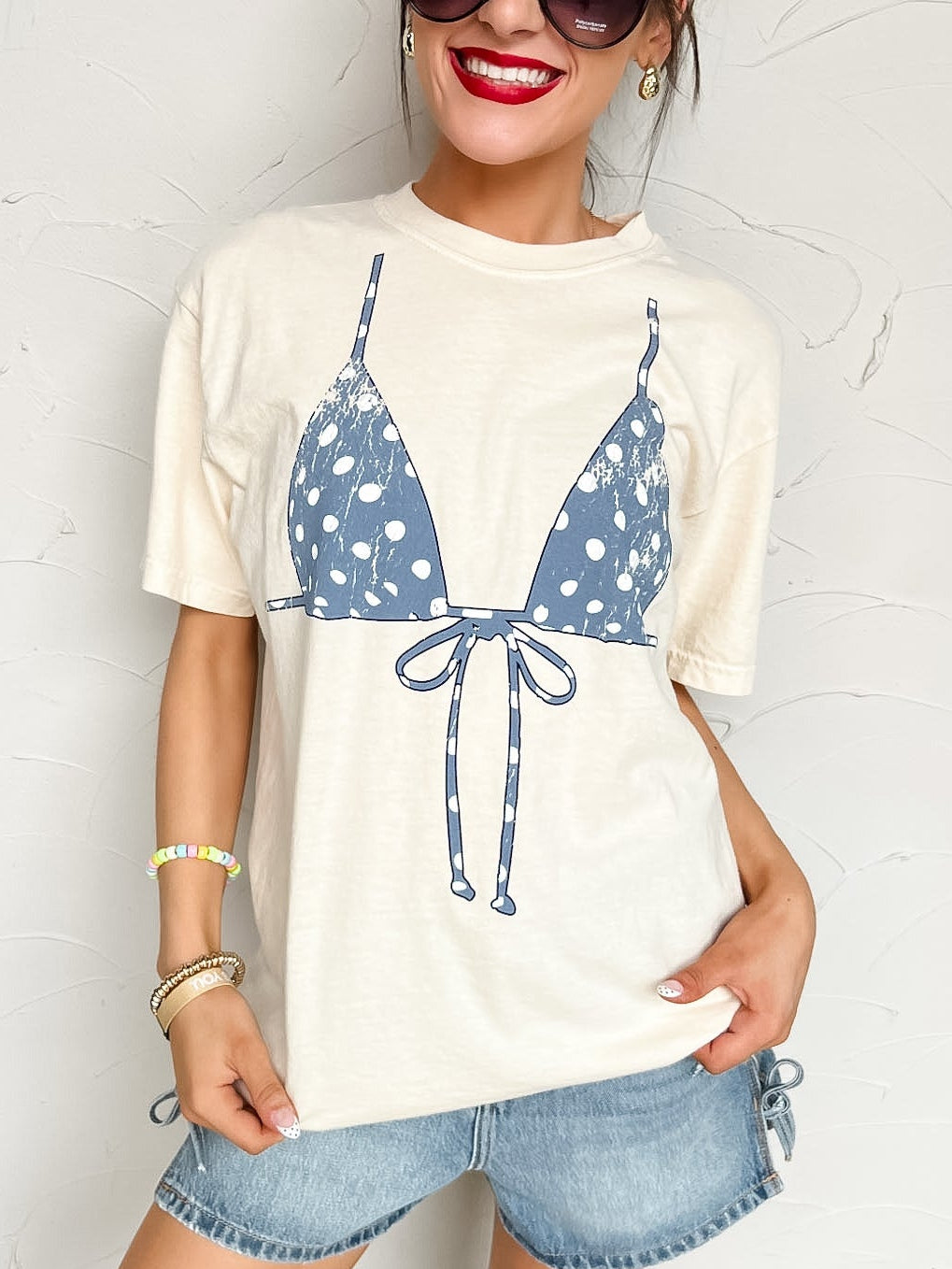 Woman wearing a white t-shirt with a blue bikini graphic and denim shorts against a white background