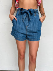 Girl in denim shorts in front of plain wall 