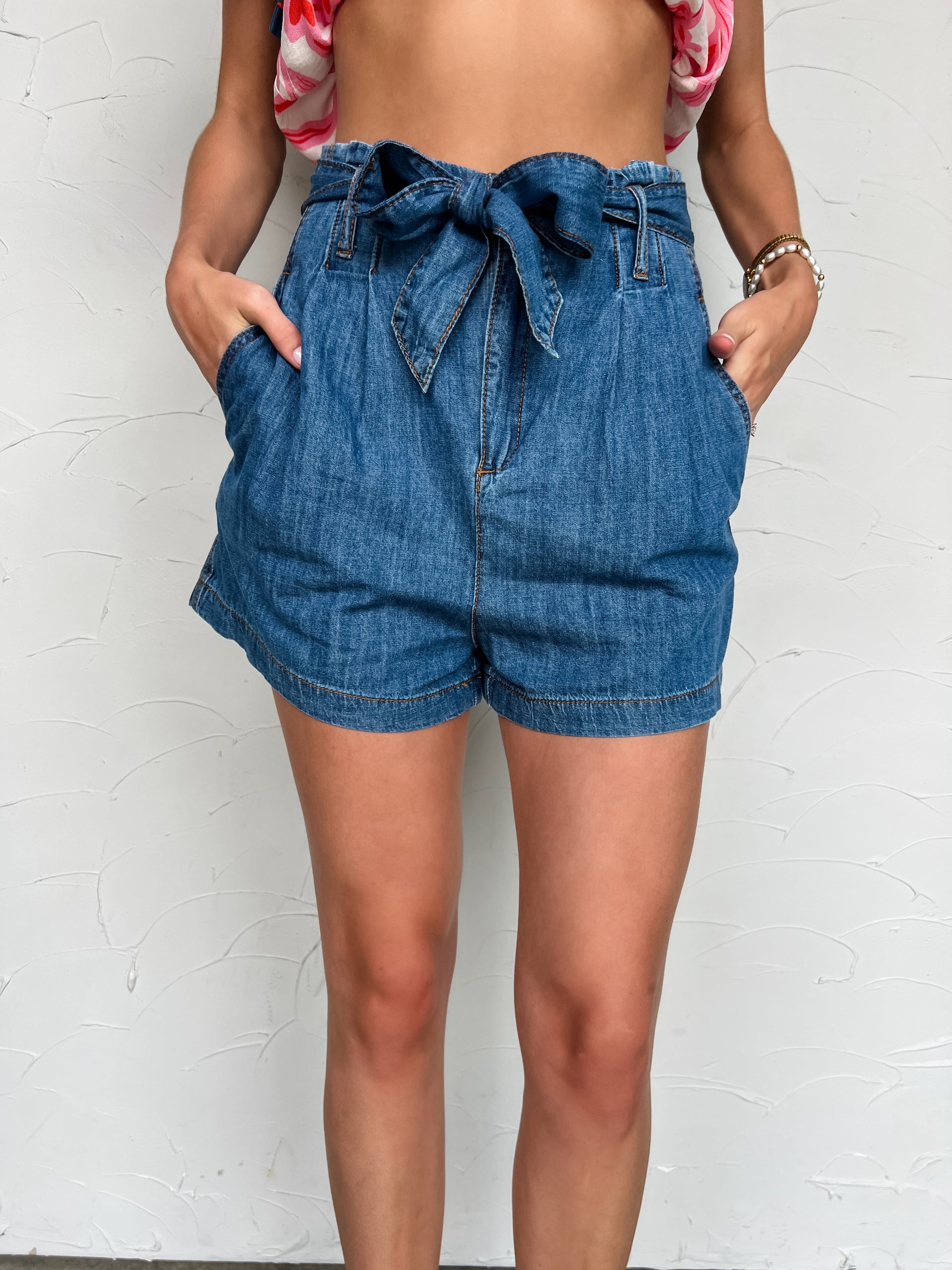 Girl in denim shorts in front of plain wall 