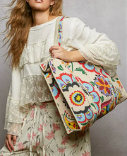 Woman holding a colorful embroidered bag against a neutral background