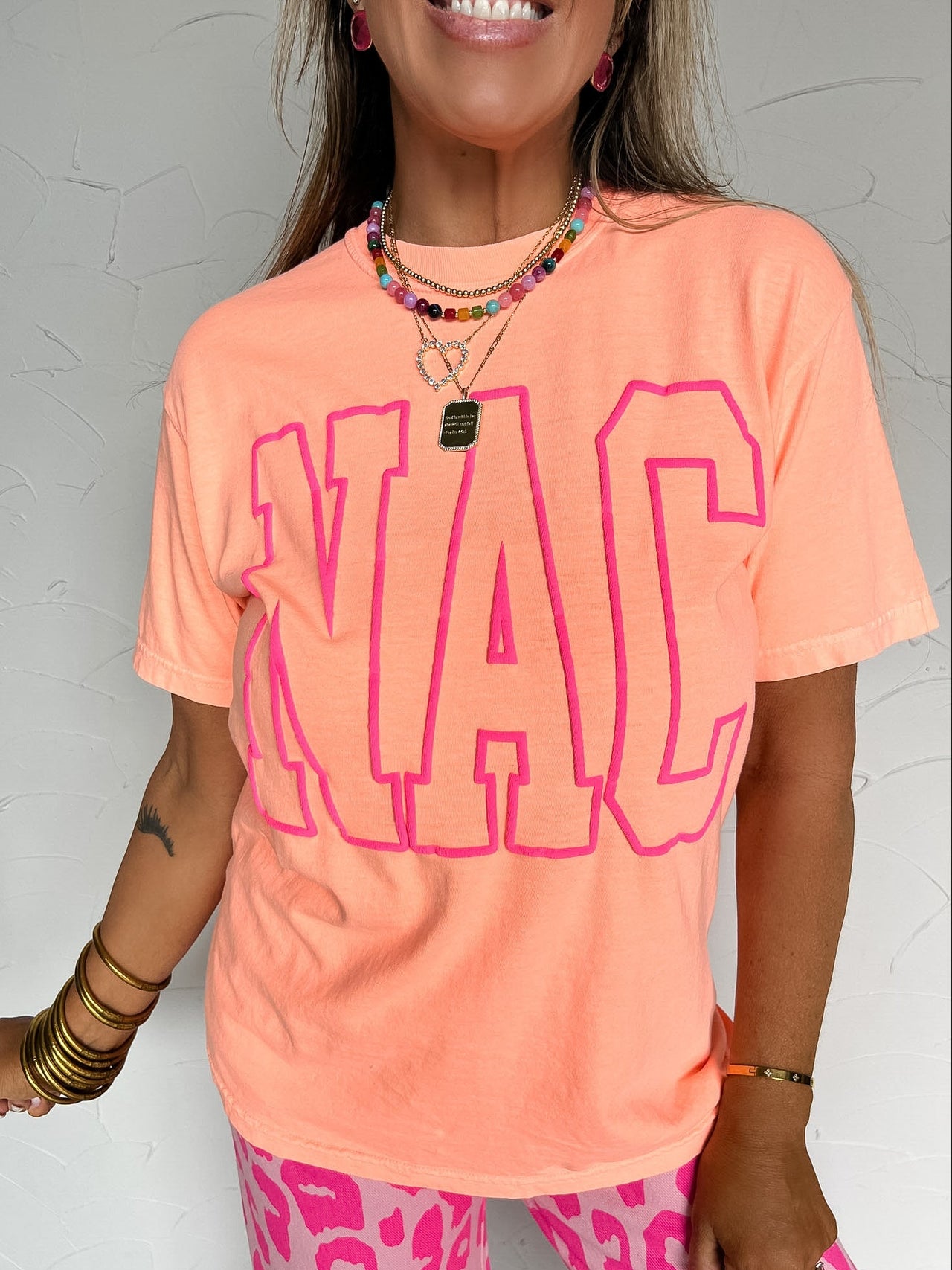 Person wearing a bright orange t-shirt with pink text and pink leopard print pants against a gray background