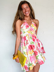 Woman wearing a floral halter neck short dress holding a yellow clutch against a white background
