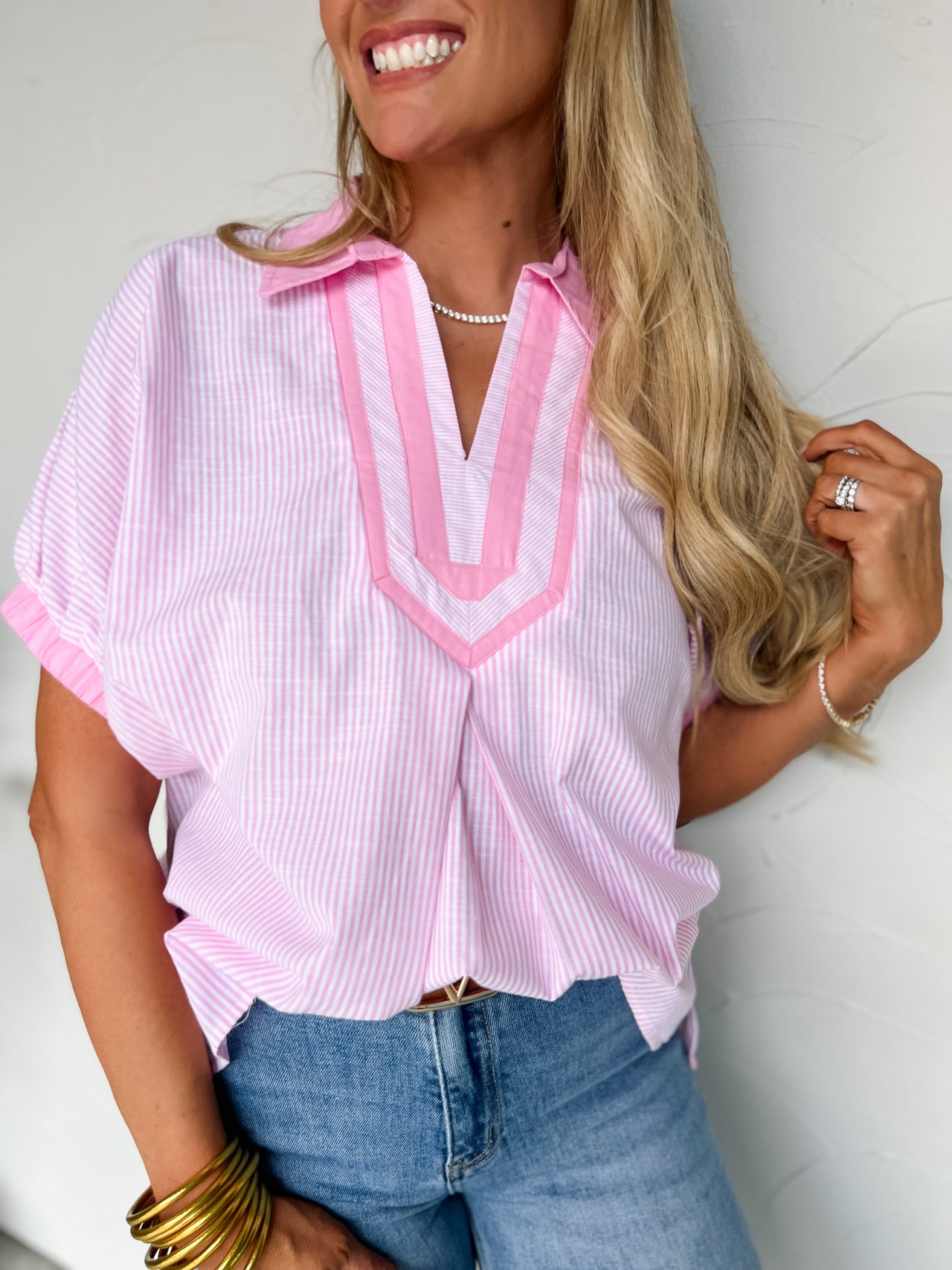 Woman wearing a pink and white striped shirt with a V-neckline, standing against a plain background.