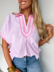 Woman wearing a pink and white striped shirt with a V-neckline, standing against a plain background.