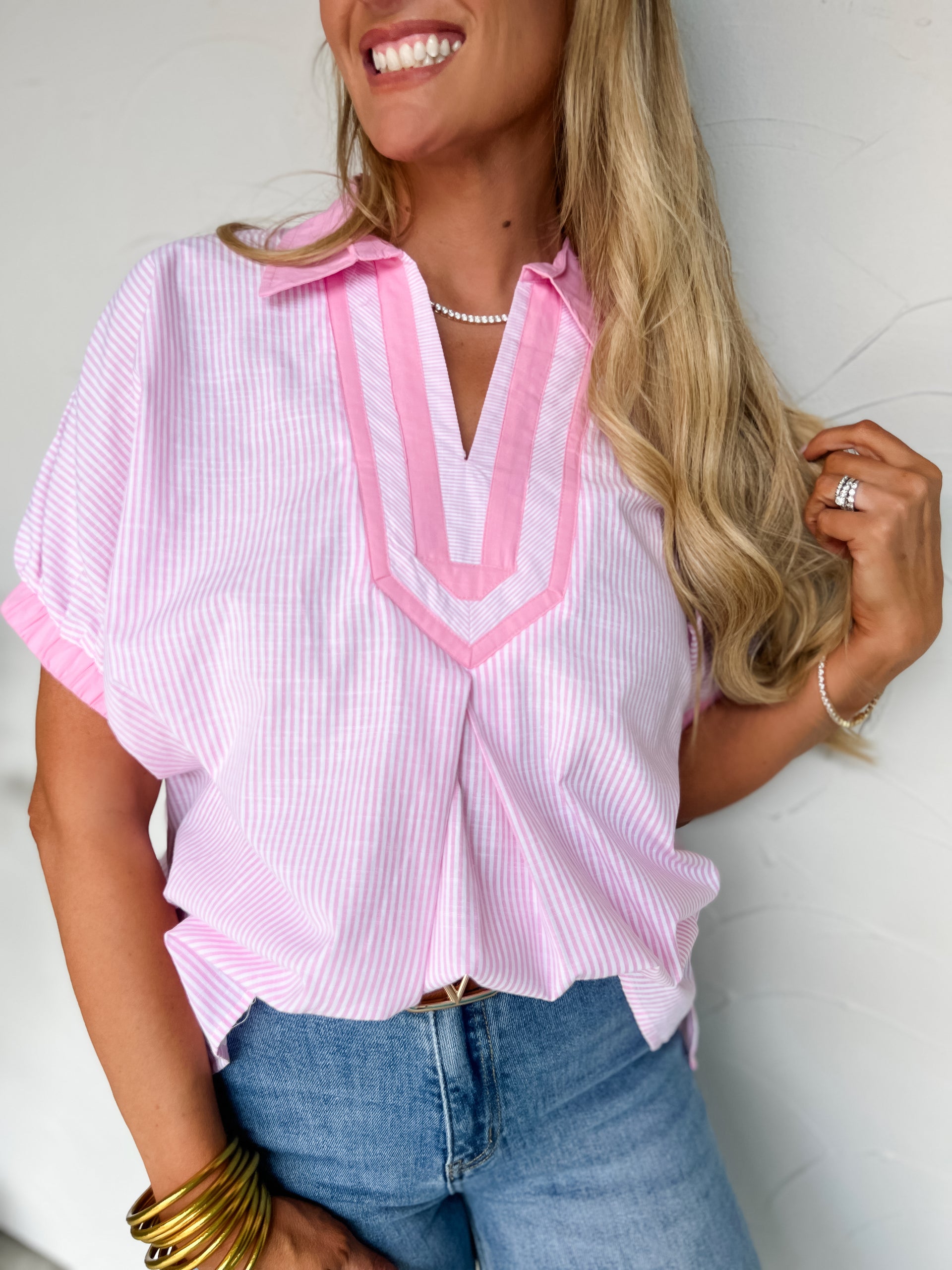Woman wearing a pink and white striped shirt with a V-neckline, standing against a plain background.