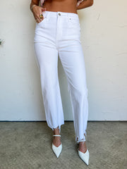Person wearing white jeans and white shoes against a plain background