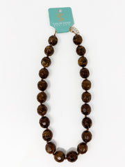 A beaded necklace made of large, polished brown faceted beads with a gold-toned clasp, hanging from a turquoise card that reads 'Taylor Made Design' on a white background.