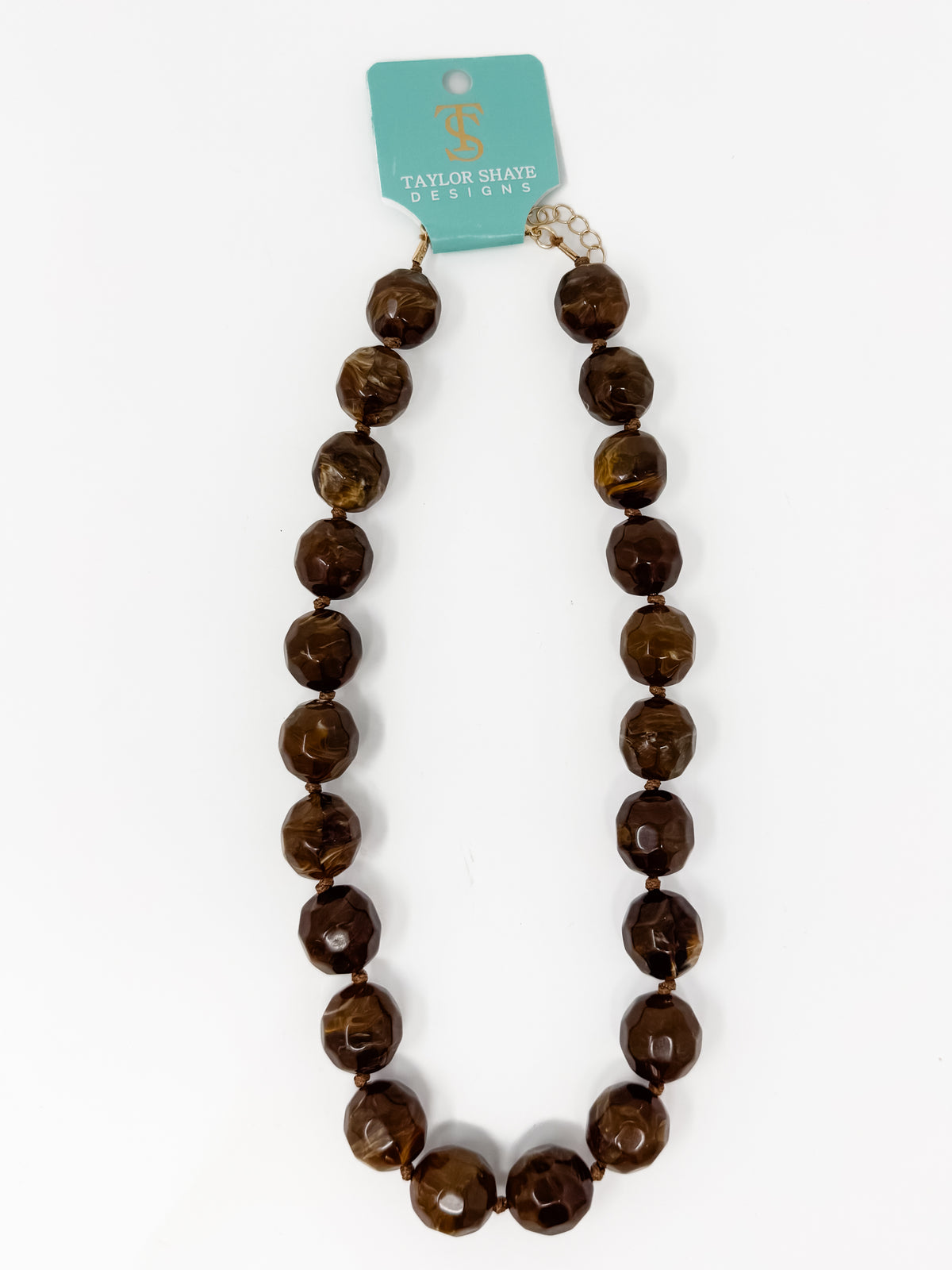 A beaded necklace made of large, polished brown faceted beads with a gold-toned clasp, hanging from a turquoise card that reads 'Taylor Made Design' on a white background.