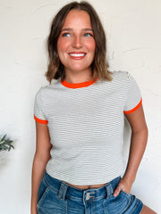 Woman wearing a striped shirt with orange trim against a white wall