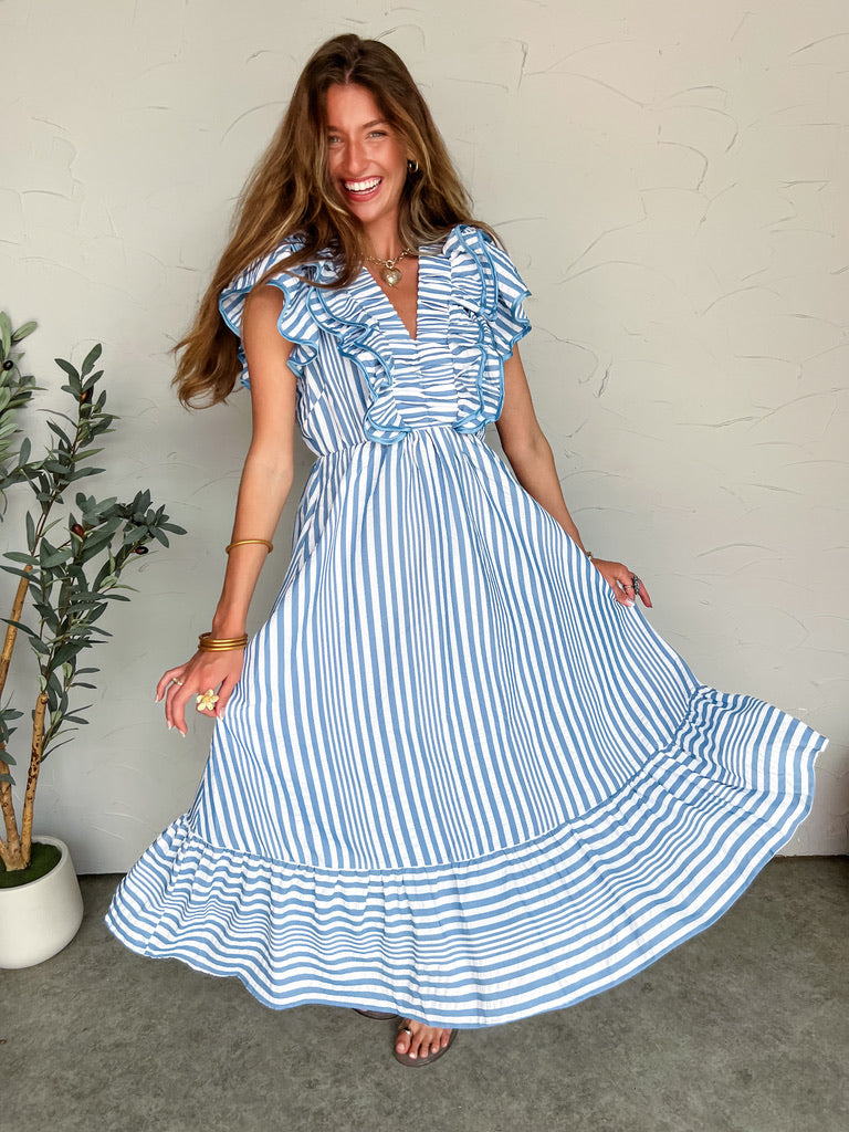 Woman wearing a blue and white striped dress against a plain wall.