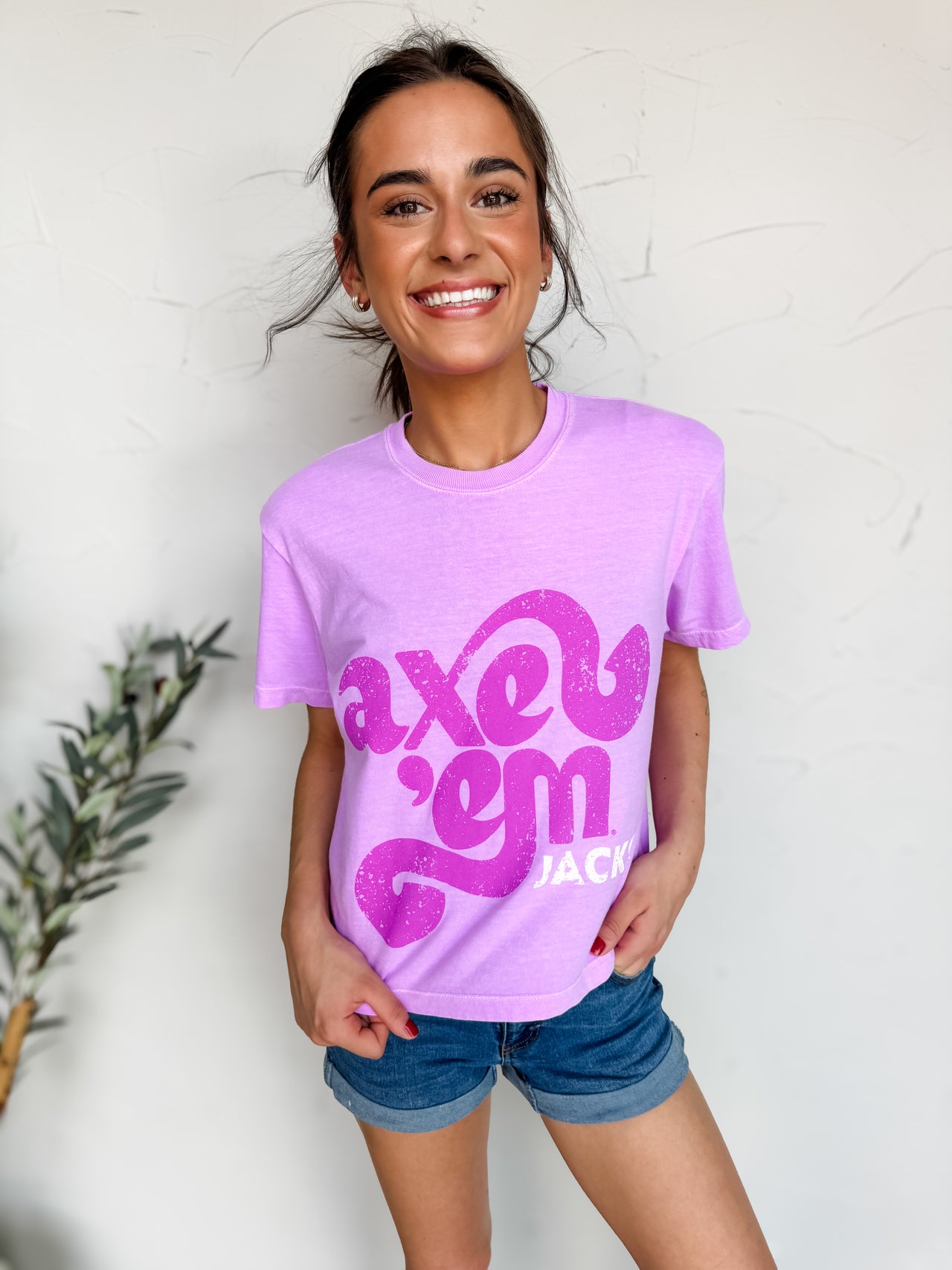 Woman wearing a purple t-shirt with pink text against a white wall