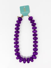 A purple beaded necklace with glossy, rounded disc-like beads, displayed on a white background with a teal brand tag that reads 'Taylor Shape Design'.