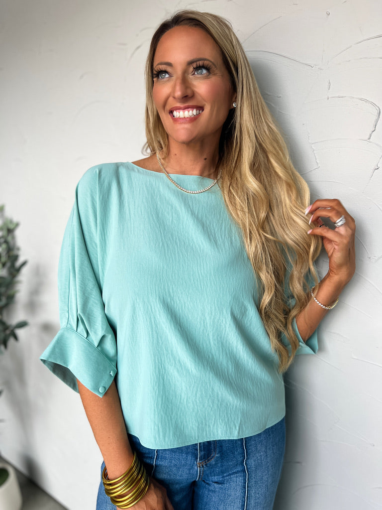 Woman wearing a light blue top and jeans against a white wall.