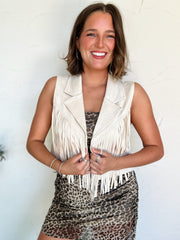 Woman wearing a white fringe vest over a leopard print dress against a light background