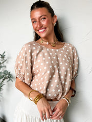 Woman wearing a beige blouse with white polka dots against a light background