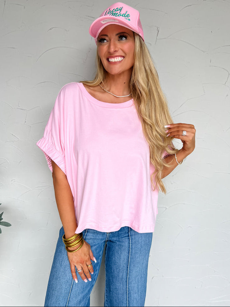 Woman wearing a pink top, jeans, and a pink cap with text on a plain background