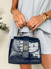 Person holding a navy blue handbag with white crocodile pattern