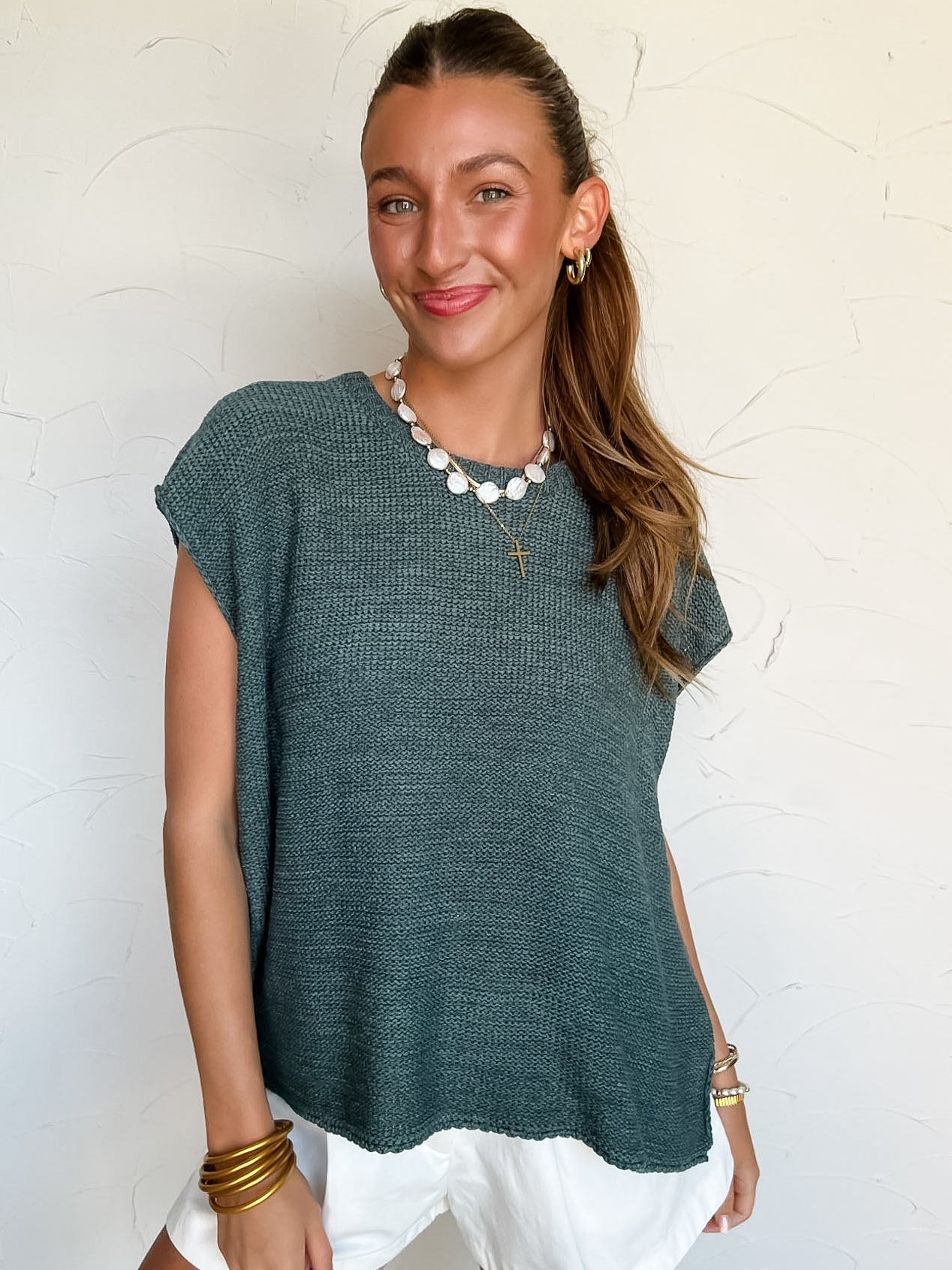 Woman wearing a green knit top and white shorts against a light background