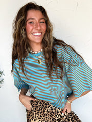 woman wearing a blue striped top with leopard pants against a white wall