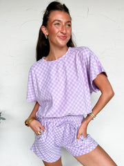 Woman wearing a matching lavender checkered top and shorts set against a white background.