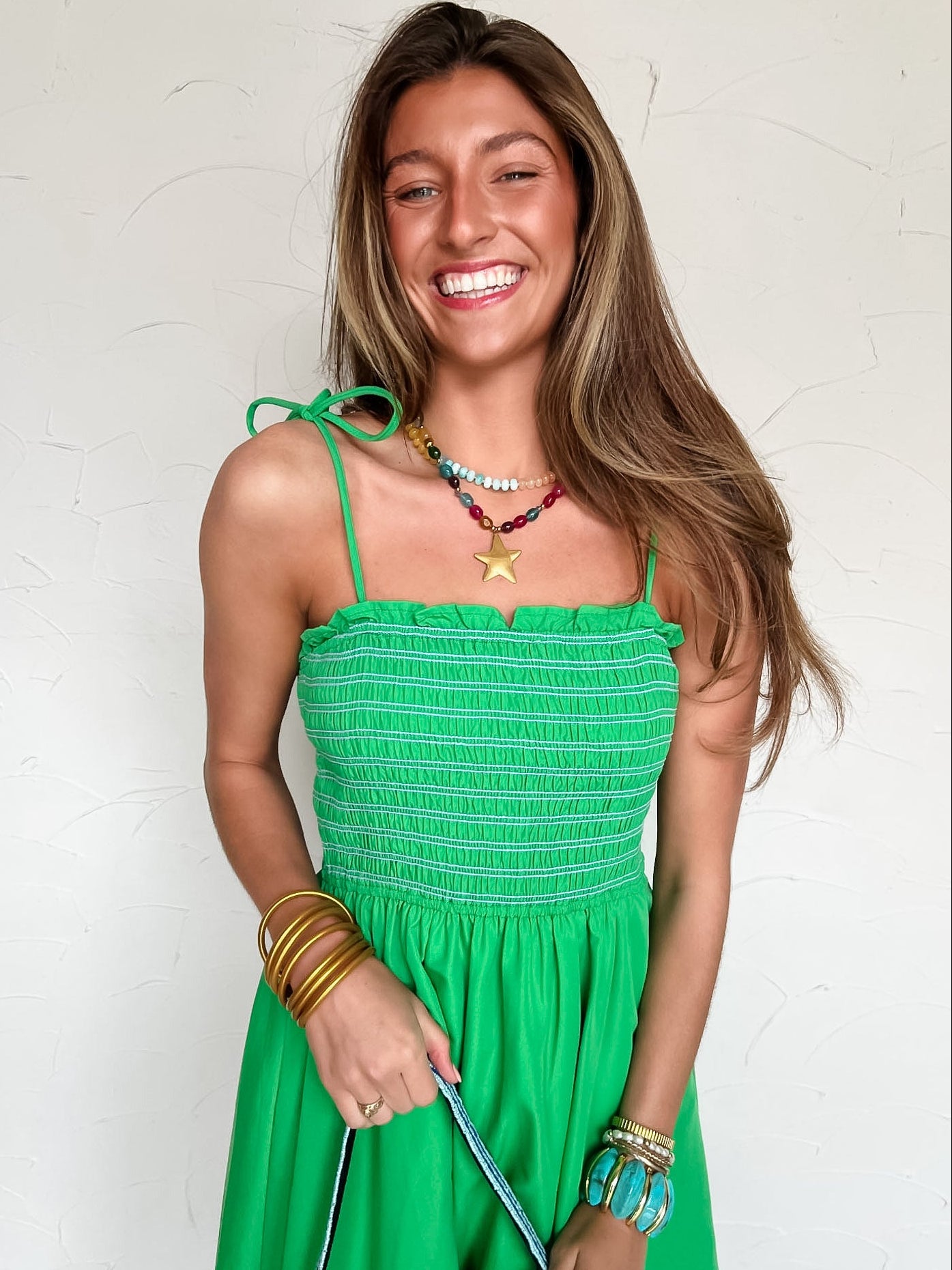 A woman wearing a green midi dress with blue accents against a white wall