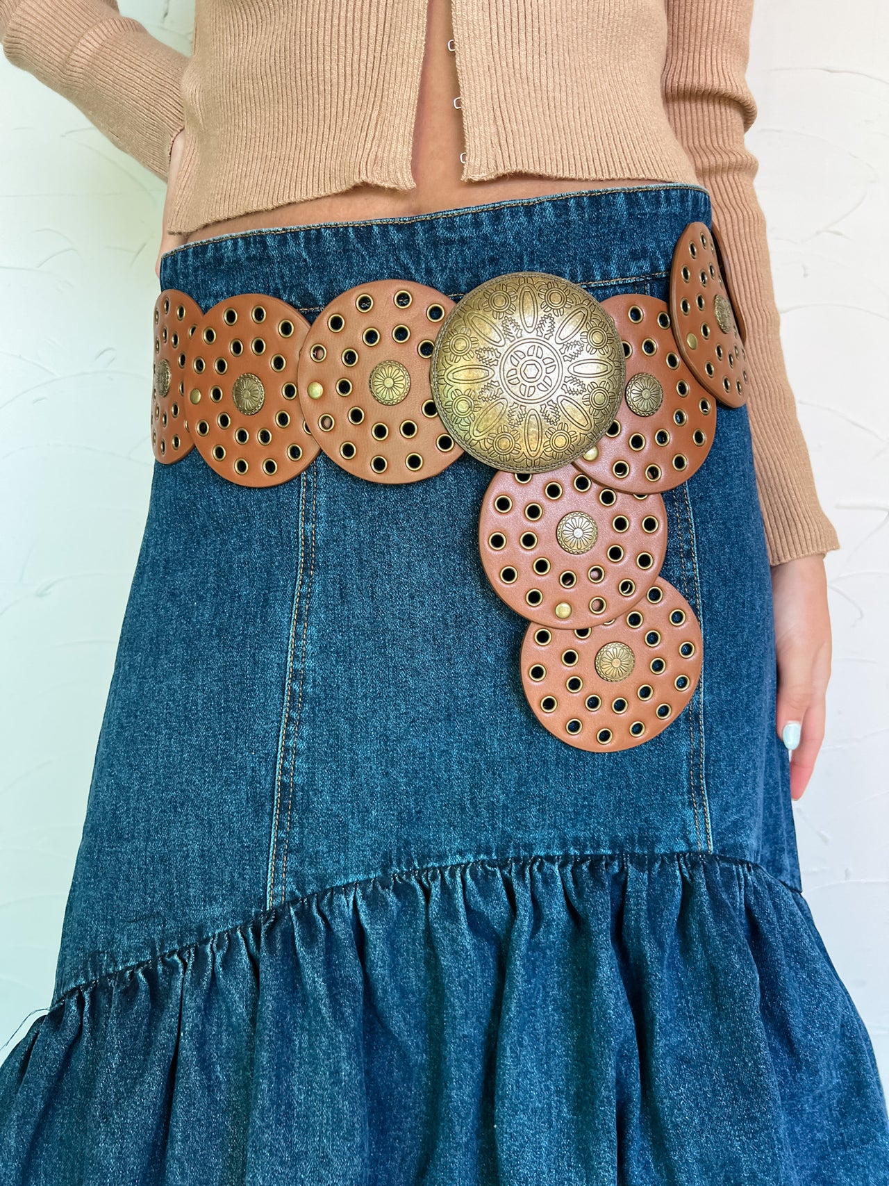 Model wearing a Western-inspired belt with faux-leather discs and an antique gold center over a denim skirt.