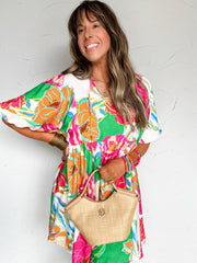 woman wearing a colorful floral mini dress with a brown tote against a white wall