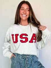 Woman wearing a grey sweatshirt with 'USA' printed in red on a plain background