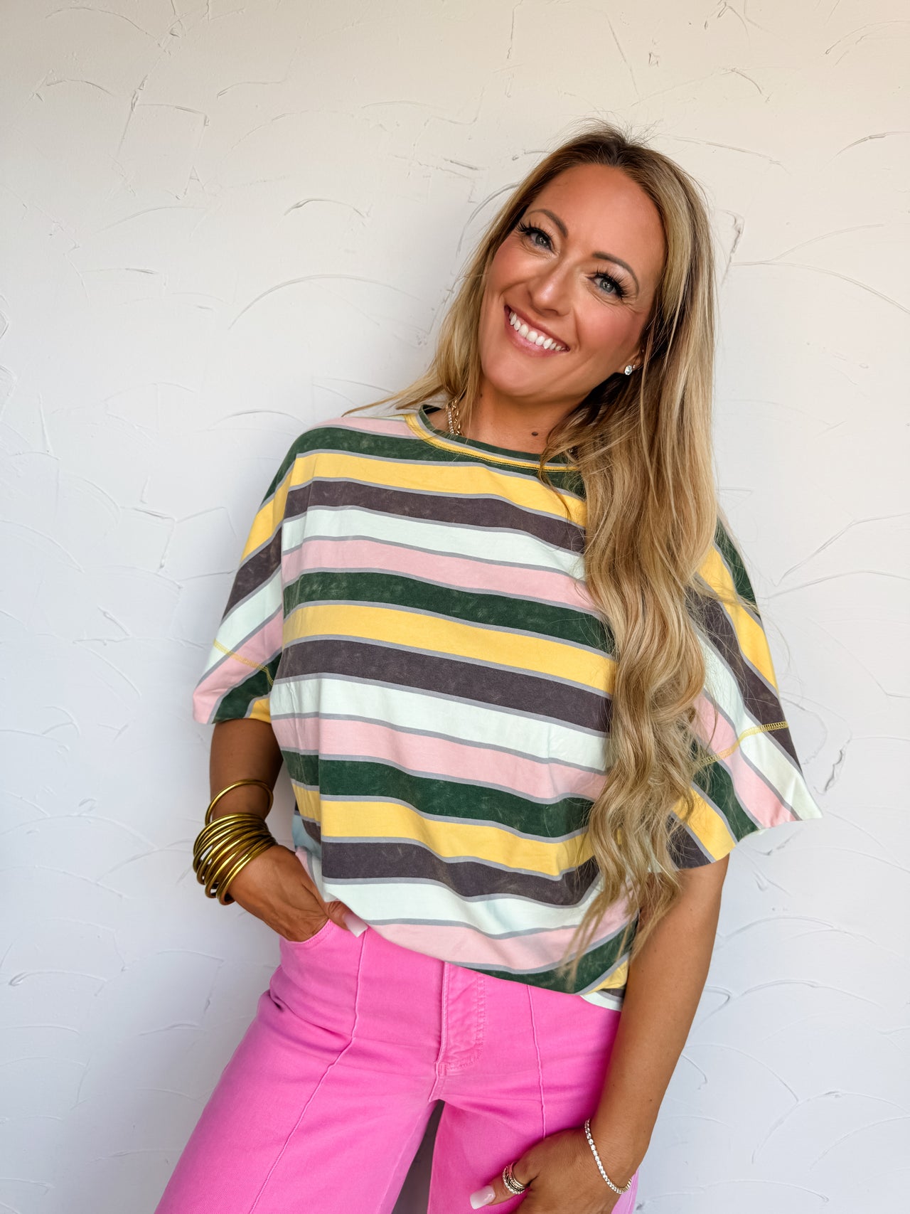 Woman wearing a colorful striped sweater and pink pants against a white wall