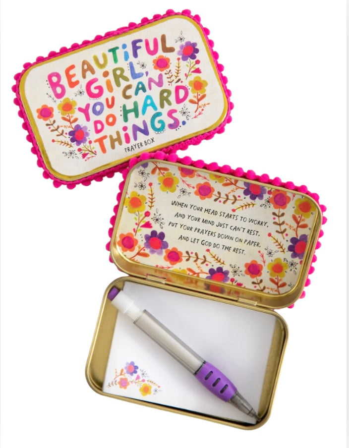 Decorative tin box with motivational quote and a note pad with a pen on a white background