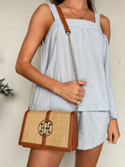 Person wearing a light blue sleeveless top and shorts, holding a woven handbag with a visible brand logo.