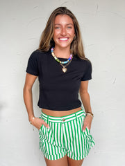 Woman wearing a black crop top and green striped shorts against a white background