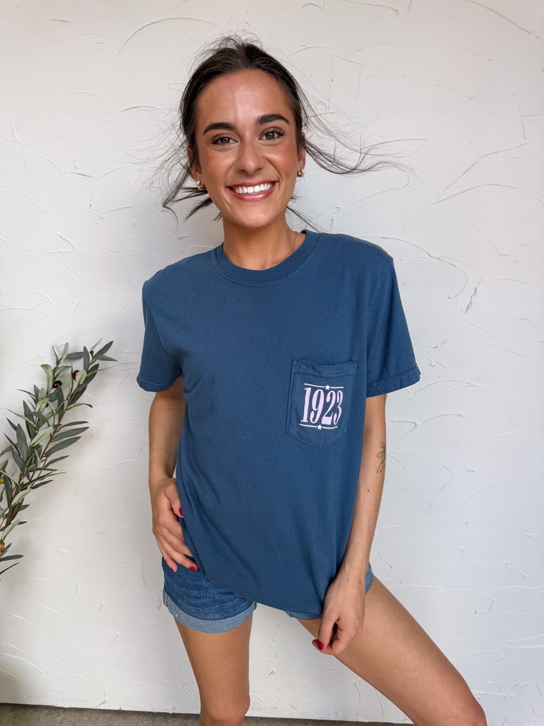 Woman wearing a blue t-shirt with a logo, standing against a white wall.