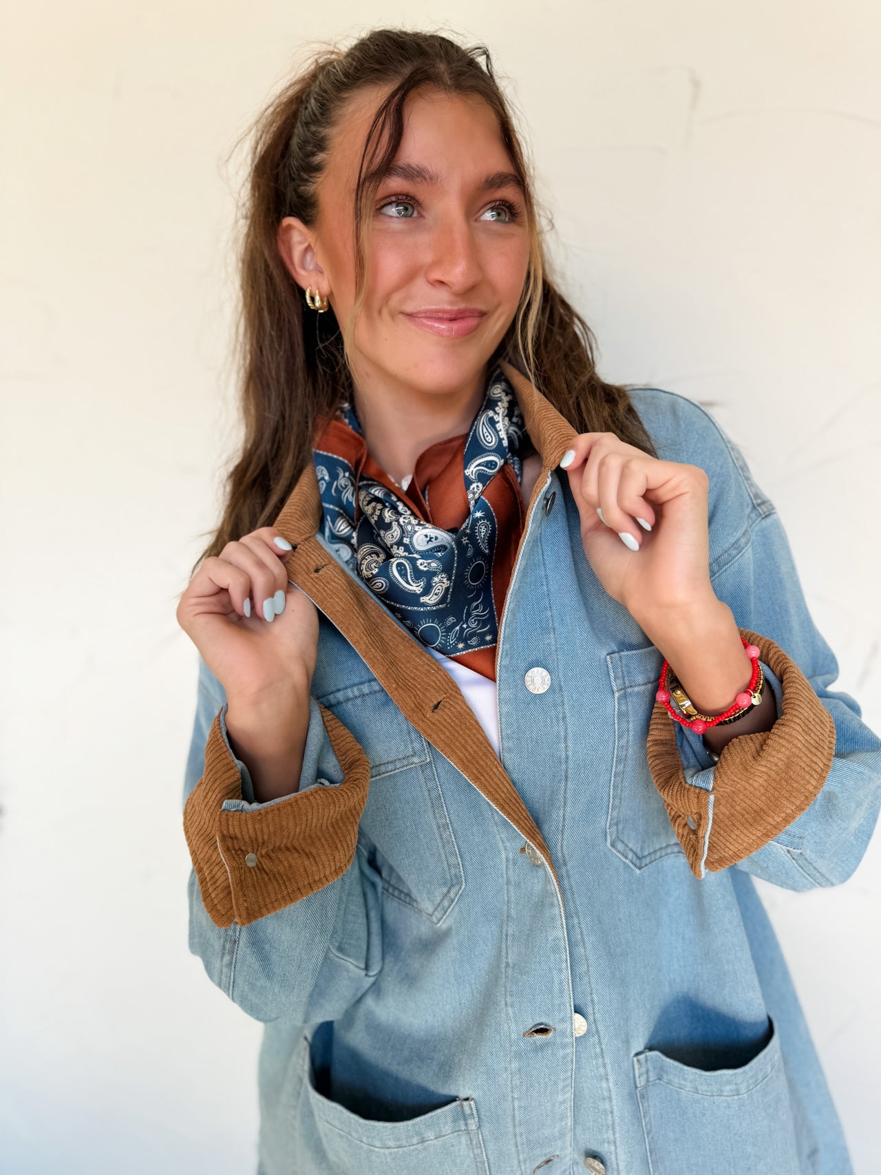 Woman wearing a denim jacket with brown corduroy collar and cuffs against a white wall
